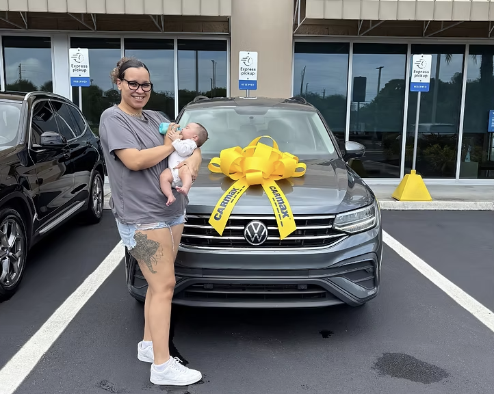 Mother holding baby next to new car with big yellow bow
