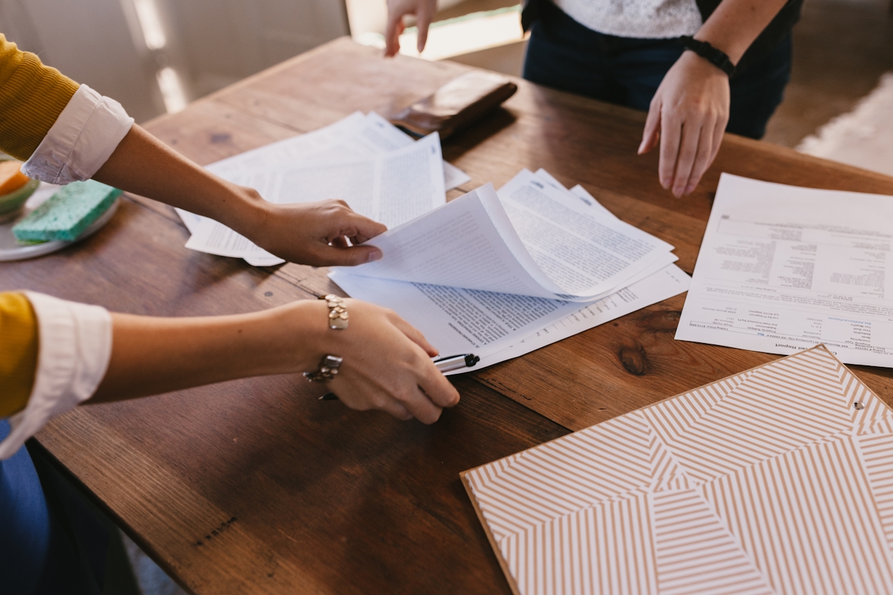 Two people's arms standing at a table going through documents