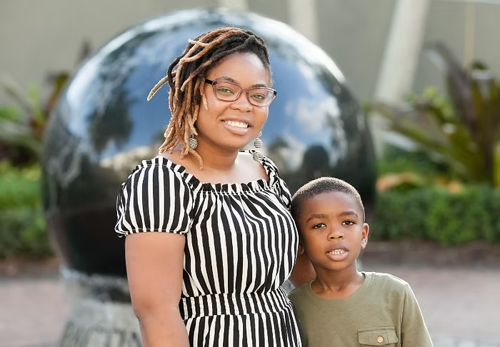 Lovely, a determined mother, smiling with her young son. She overcame challenges to pursue her dream of becoming a Registered Nurse through support from Hearts For Moms