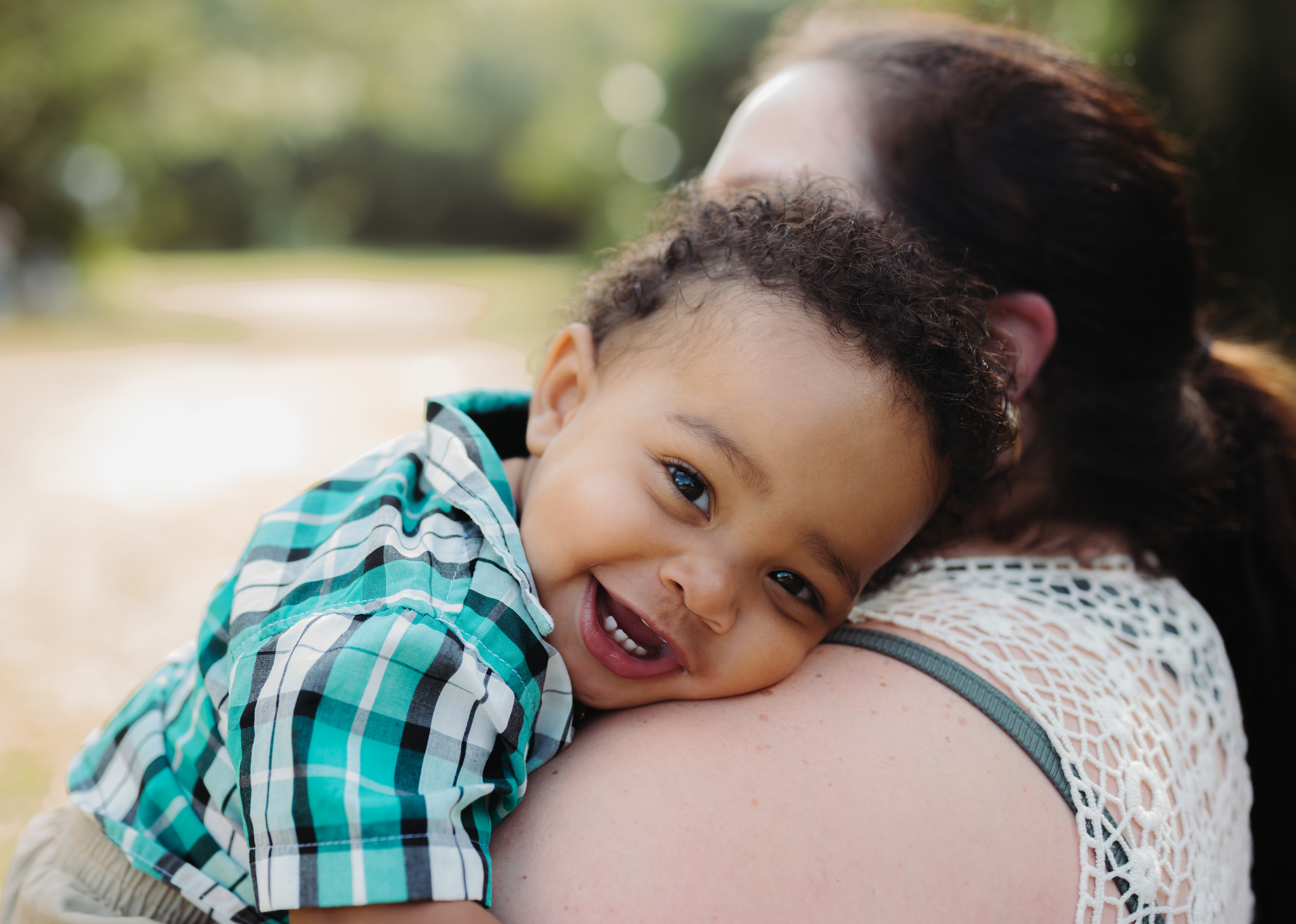 Close up of baby smiling held against Mother's shoulder, looking into camera